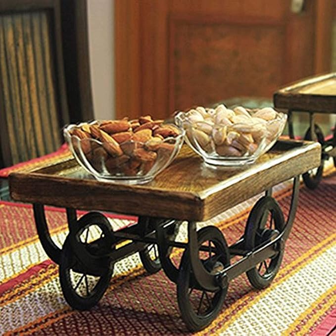 Wooden serving cart with wheels on a striped rug, containing glass bowls of snacks.